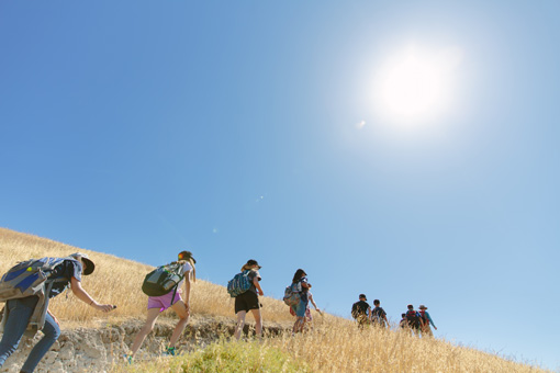 Photograph of a large group of students ascending a hill on a sunny day, brown grasslands on either edge of the trail.