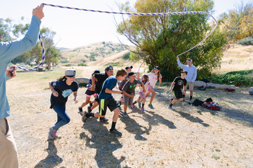 Photograph of a group of eight children all playing jump rope at the same time. The rope ends are held by their principal and a teacher.
