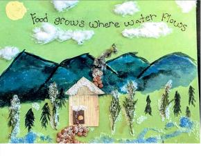 A photo of a mixed media art project on green construction paper. A painted yellow sun in the top left. Wispy cotton ball clouds in the sky. A quote among the clouds: "Food grows where water flows." Below are painted mountains, a house made of cornhusks, with a chimney and sidewalk of lentils, surrounded by trees of pine leaves and snow made of salt.